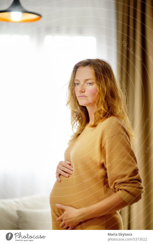 Schwangere kaukasische Frau entspannt sich zu Hause. Junge werdende Mutter streichelt ihren schwangeren Bauch und denkt über das Baby Geburt. Konzept der Mutterschaft und Schwangerschaft