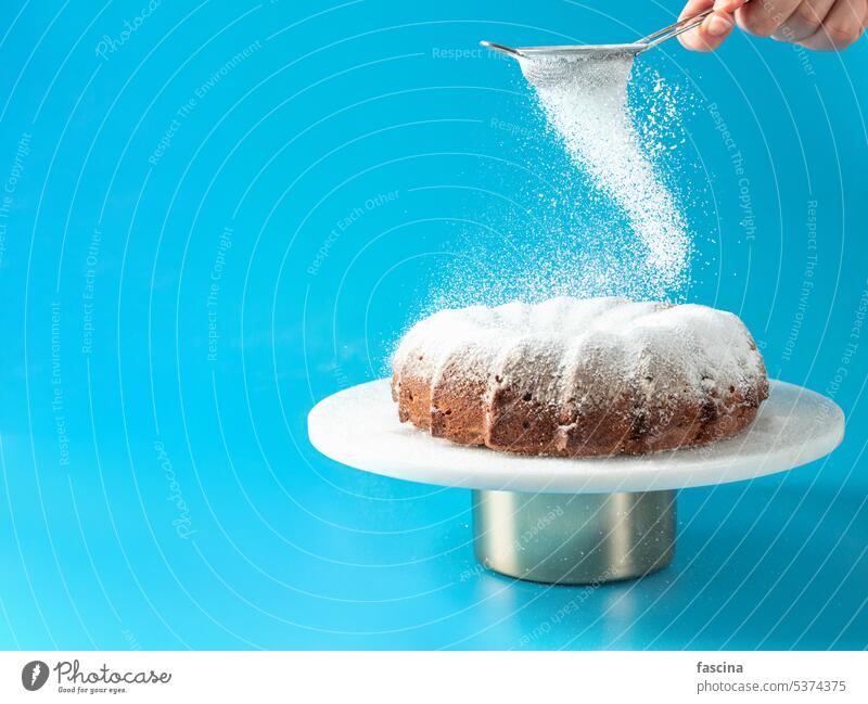 Weibliche Hand, die Puderzucker auf einen Gugelhupf streut Bundkuchen Blechkuchen Kuchen Zucker fallend Zuckerguß hausgemacht blau selbstgemacht heimwärts
