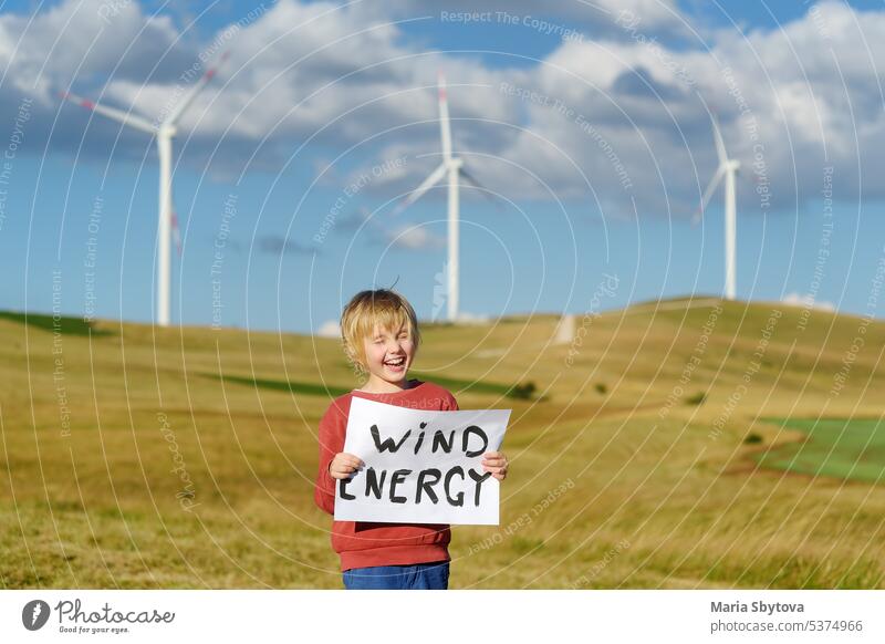 Öko-Aktivist Junge mit Banner "Windenergie" auf dem Hintergrund von Kraftwerken für erneuerbare elektrische Energieerzeugung. Kind und Windmühlen. Windturbinen zur Stromerzeugung. Grüne Energie