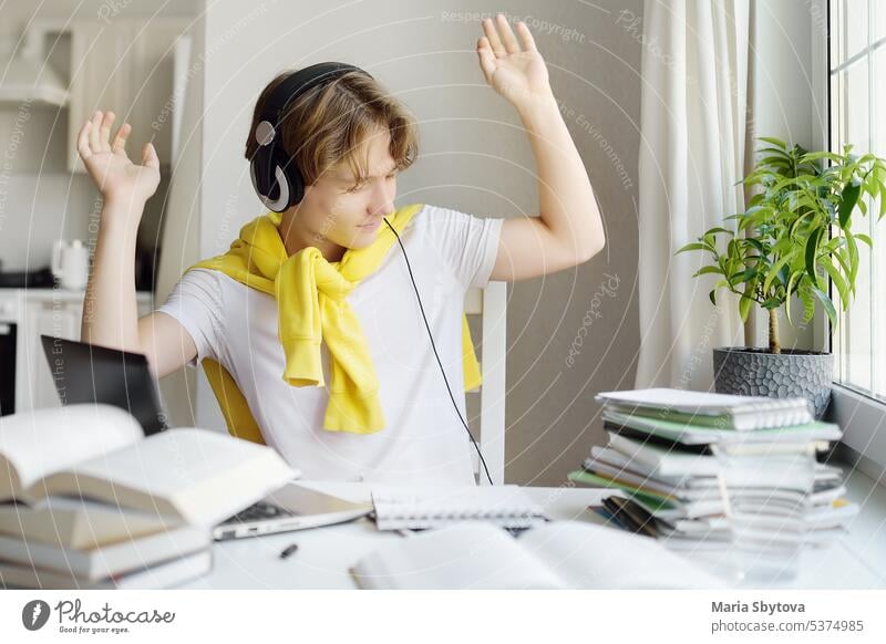 Teenager-Junge lernt zu Hause mit Gadgets. Online-Bildung und Fernunterricht für Kinder. Gymnasiast trägt Kopfhörer Musik hören, tanzen und Freude, weil Hausaufgaben Test getan.
