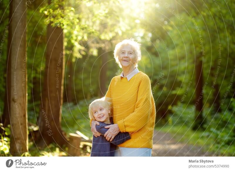Liebevoller Enkel umarmt zärtlich seine fröhliche ältere Großmutter beim Spaziergang im Sommerpark. Zwei Generationen einer Familie. Senior alt Kind Umarmung