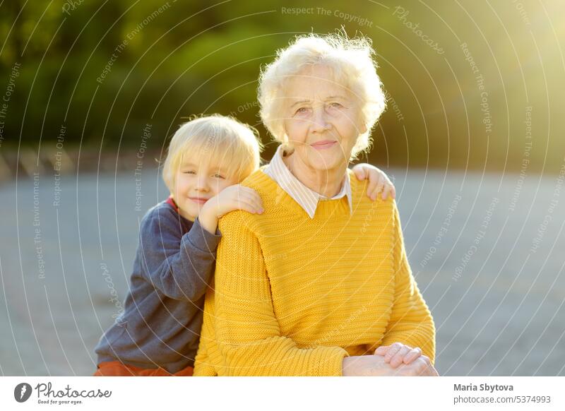 Liebevoller Enkel umarmt zärtlich seine fröhliche ältere Großmutter beim Spaziergang im sonnigen Sommerpark. Zwei Generationen einer Familie. Senior alt Kind