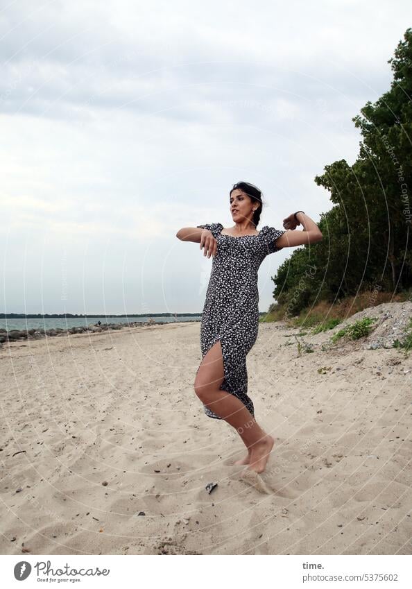 Frau am Strand, einen Stein Richtung Wasser werfend Ostsee Kraft Bewegung Kleid dunkelhaarig langhaarig Zopf Sand Spaß Wurfvorbereitung Wald Horizont Himmel