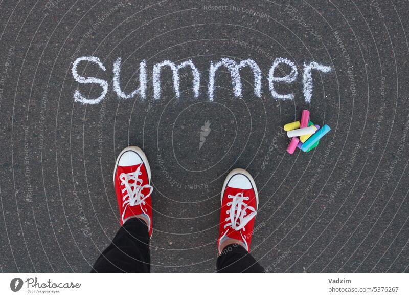 Draufsicht auf das Wort Sommer, geschrieben mit weißer Kreide auf dem Bürgersteig, farbige Kreide und Beine in roten Turnschuhen. Asphalt farbenfroh Buntstifte