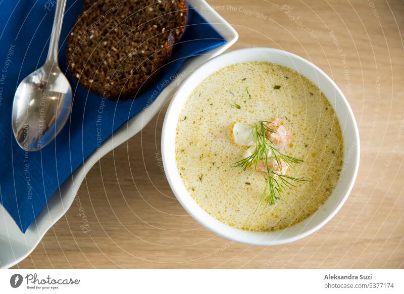Eine Schüssel mit finnischer Lohikeitto-Suppe, serviert auf einem Holztisch mit einem Stück schwedischem Roggenbrot. Cremige Brühe, zarte Kartoffeln und flockiger rosa Lachs ergeben ein köstliches Gericht.