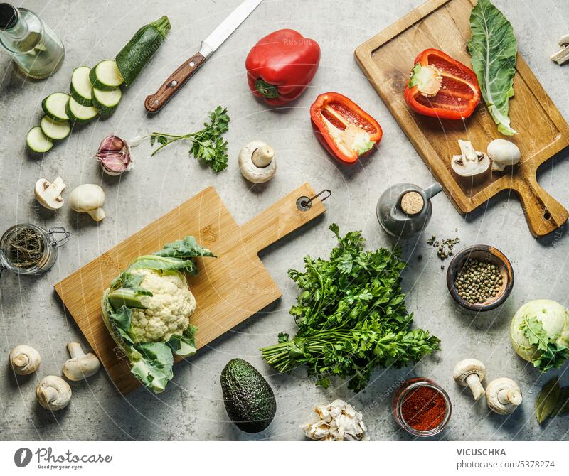 Verschiedene gesunde Gemüse Zutaten auf Küche Schreibtisch Hintergrund mit Messer, Kräuter, Gewürze und Schneidebretter. Ansicht von oben. Veganes Essen