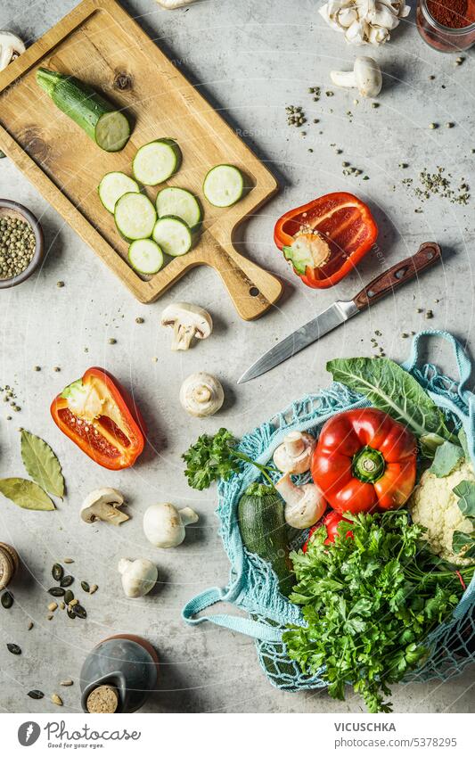 Gesundes Kochen mit verschiedenen frischen Gemüsesorten auf dem Küchentisch mit Messer, Schneidebrett und nachhaltiger Netztasche mit Lebensmitteln. Ansicht von oben