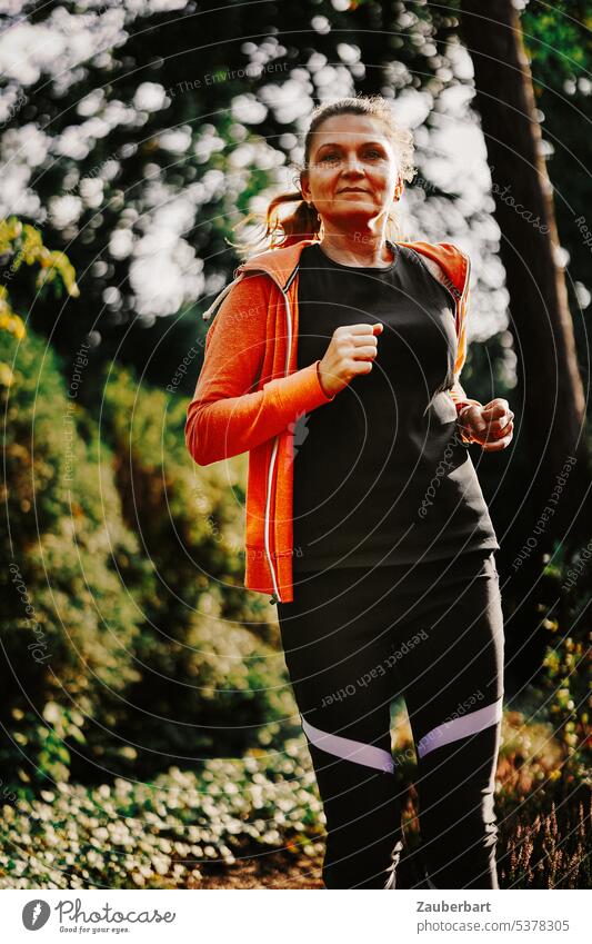Frau beim Joggen im Wald joggen Sport laufen Natur orange Gegenlicht Fitness sportlich Gesundheit Training Lifestyle Läufer rennen schön üben Erwachsene