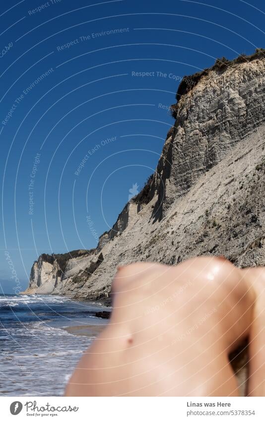 Ein wunderschöner Strand in Korfu, Griechenland. Eine wilde Küste und ruhiges Meer. Ein blauer Himmel. Und ein wunderschönes nacktes Mädchen, das unscharf ist. Ihre sexy, verschwommenen Linien sind jedoch unübersehbar. Eine junge, nackte Frau genießt offensichtlich den heißen Sommer.