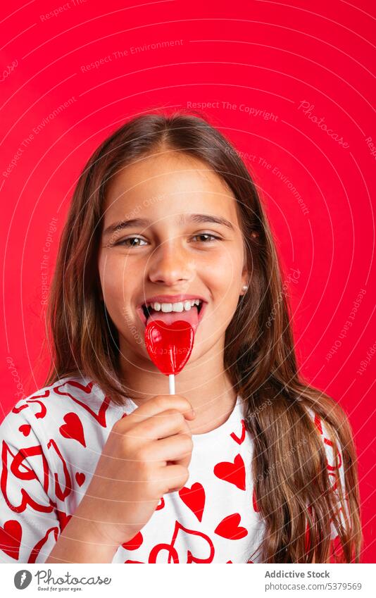 Niedliches kleines Mädchen leckt roten Lutscher Porträt Bonbon süß Lollipop lutschen positiv Lächeln Glück Kind bezaubernd niedlich lässig Kindheit lange Haare