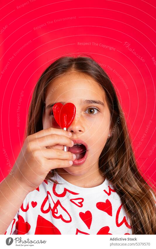 Überraschtes Mädchen mit offenem Mund leckt Lutscher mit rotem Herz Lollipop Überraschung erstaunt verwirren süß Bonbon Porträt Mund geöffnet Geduldsspiel Kind