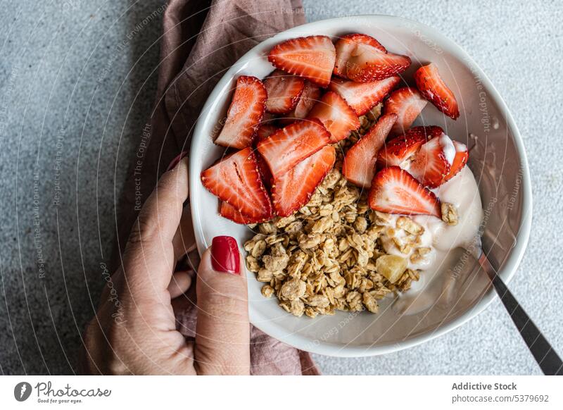 Abgeschnittene Hand hält Schüssel mit gesundem Frühstück mit Erdbeeren, Joghurt und Müsli Frau Beteiligung Hintergrund Beeren Schalen & Schüsseln Konzept Beton