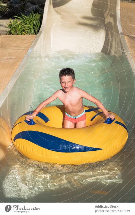 Glückliches Kind, das auf einem Ring auf der Wasserrutsche steht Sliden Spaß haben genießen Park nasses Haar aufblasbar Lächeln Junge Sommer Wochenende Kindheit