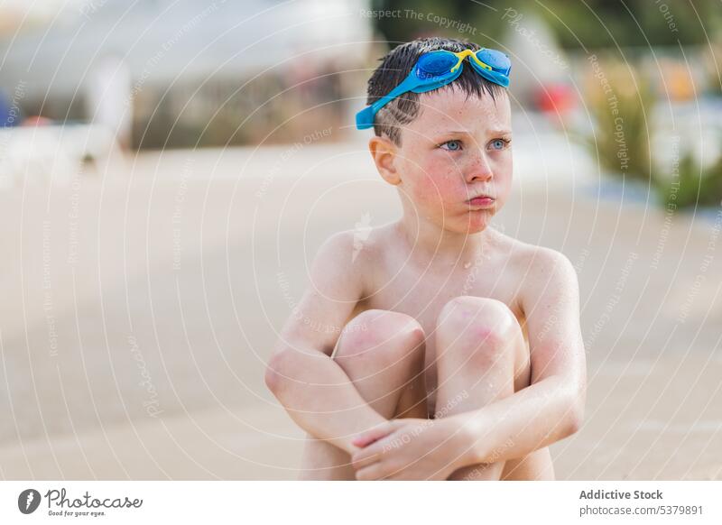 Kind sitzt auf dem unscharfen Boden des Parks Fokus ohne Hemd Windstille Schutzbrille niedlich nass nackte Schultern Sommer Junge Erholung Wochenende tagsüber