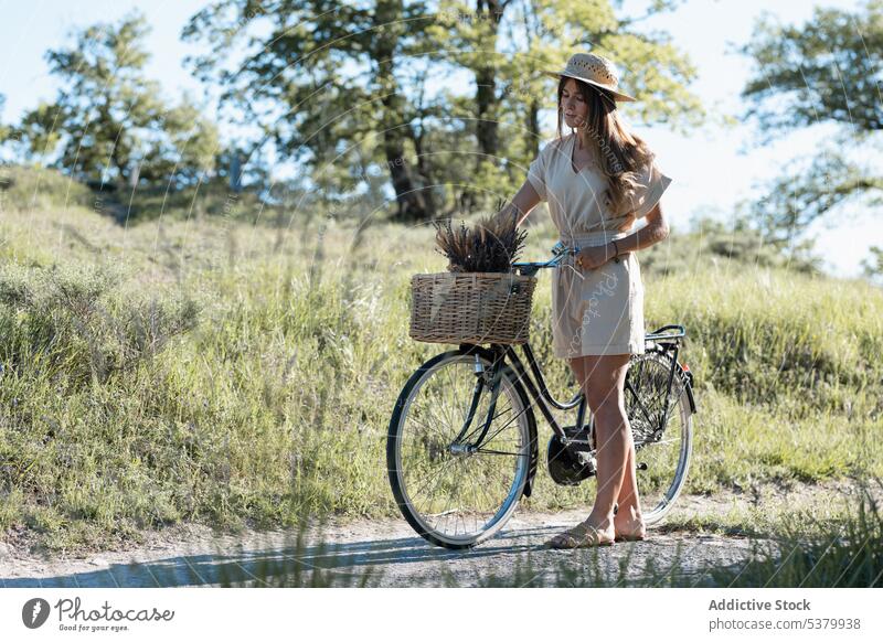 Junge Frau mit Fahrrad in der Natur stehend Strohhut Weide Korb Weizen Spitze Schatten Landschaft Sommer jung Stil ländlich Sonne Straße Sommerzeit außerhalb