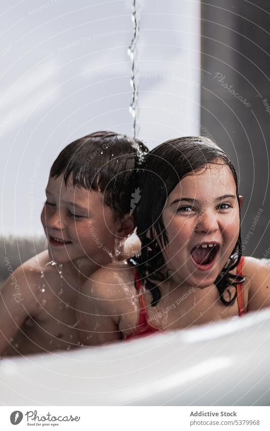Glückliche Kinder haben Spaß im Pool unter fallendem Wasser Geschwisterkind heiter Badewanne Lächeln Spaß haben Mund geöffnet genießen Badebekleidung aufgeregt