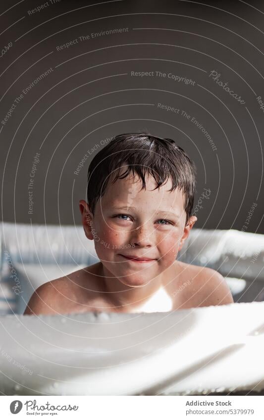 Niedliches Kind mit nassen Haaren im aufblasbaren Pool sitzend Porträt Lächeln nasses Haar aufblasbarer Pool Glück Sommer bezaubernd ohne Hemd