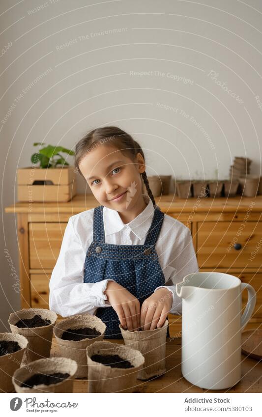Niedliches kleines Mädchen mit lehmiger Erde in flexiblen Pflanzschalen auf dem Tisch niedlich heimwärts Topf Garten positiv Arbeit Pflanze Gartenbau Boden Kind