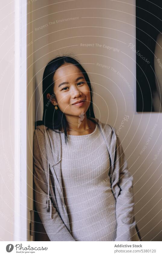Lächelnde asiatische Frau in Freizeitkleidung Raum positiv Fenster Glück ruhen heimwärts gemütlich lässig froh ethnisch jung Optimist Appartement Freude