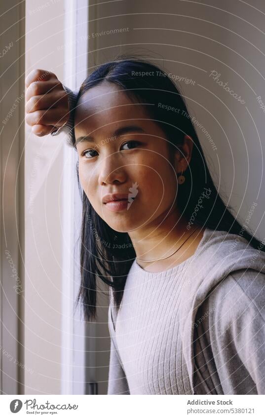 Asiatische Frau schaut in die Kamera, während sie am Fenster steht ernst Porträt selbstbewusst Windstille nachdenklich besinnlich Stil lässig asiatische Frau