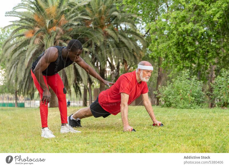 Seriöser schwarzer Trainer, der einem Mann hilft, Liegestütze auf dem Rasen zu machen Männer hochschieben Training Trainerin Übung Hilfsbereitschaft Park Sport