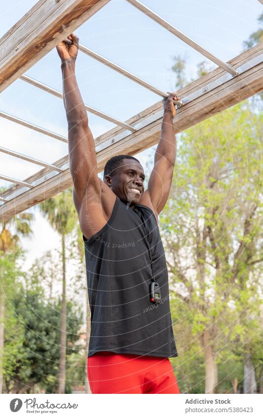 Glücklicher schwarzer Mann, der an der Bar eines Sportplatzes hängt Training ziehen Übung Athlet Sportpark stark Afroamerikaner ethnisch Straße Fitness männlich