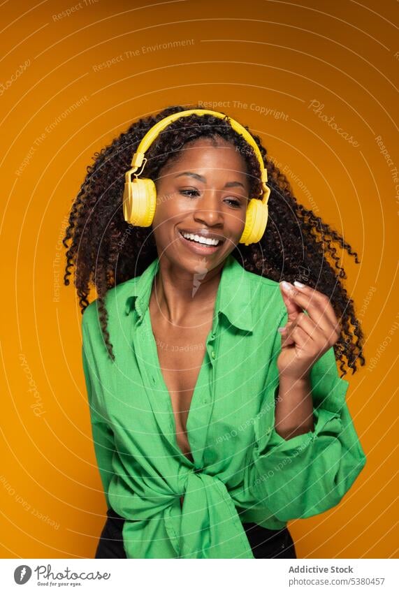 Frau mit Kopfhörern, die eine Melodie hört und tanzt Tanzen zuhören Musik Lächeln Glück orange schwarz Afroamerikaner meloman Headset Gesang Wiedergabeliste