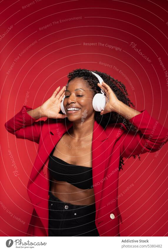 Fröhliche Frau mit Händen auf Kopfhörern zuhören Musik Drahtlos Stil Lächeln trendy Glück Melodie positiv schwarz Afroamerikaner Gesang Gerät modern meloman