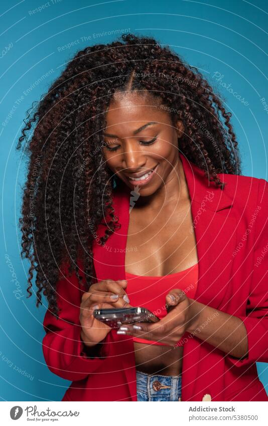 Lächelnde Frau in rotem Outfit sendet Botschaft reden Smartphone Mode Stil schwarz Texten jung Gespräch Glück Afro-Look benutzend Telefon Gerät Mobile Apparatur