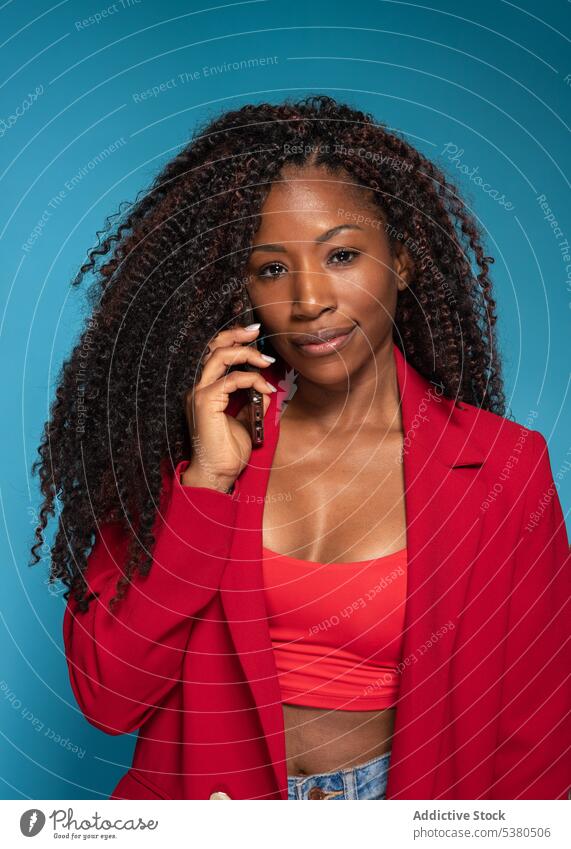 Nachdenkliche Frau in roter modischer Kleidung, die mit ihrem Smartphone spricht reden Telefonanruf sprechen Mode Stil schwarz jung Outfit Gespräch Afro-Look