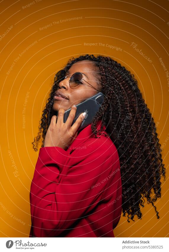 Nachdenkliche Dame, die im Studio über ihr Smartphone spricht Frau Gespräch Telefonanruf Stil trendy Outfit positiv reden Afroamerikaner schwarz jung sprechen