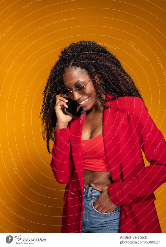 Fröhliche Dame, die im Studio mit ihrem Smartphone spricht heiter Frau Gespräch Lächeln Telefonanruf Stil trendy Outfit positiv reden Afroamerikaner Glück