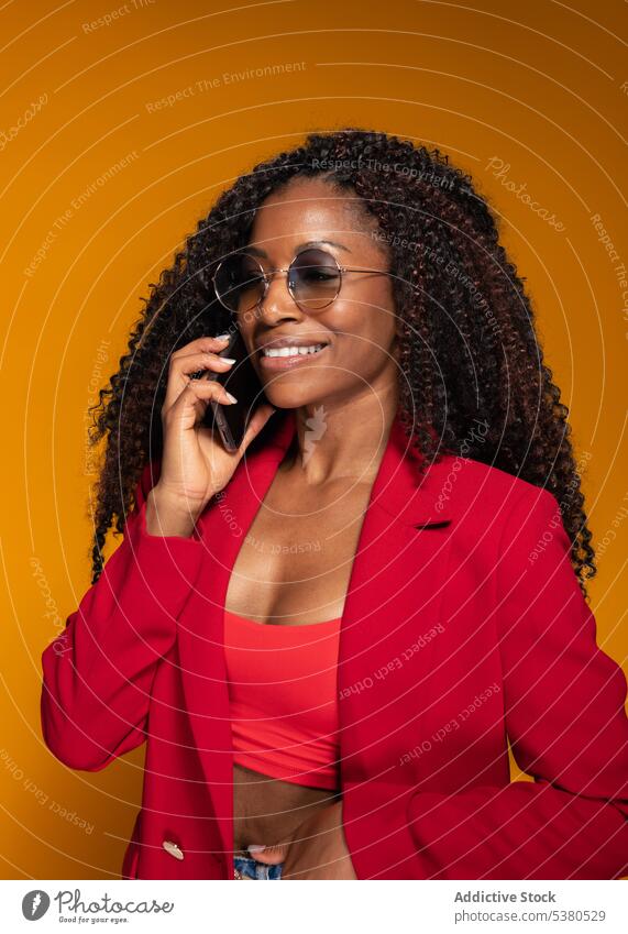 Fröhliche Dame, die im Studio mit ihrem Smartphone spricht Frau Gespräch Lächeln Telefonanruf Stil trendy Outfit positiv reden Afroamerikaner Glück schwarz jung