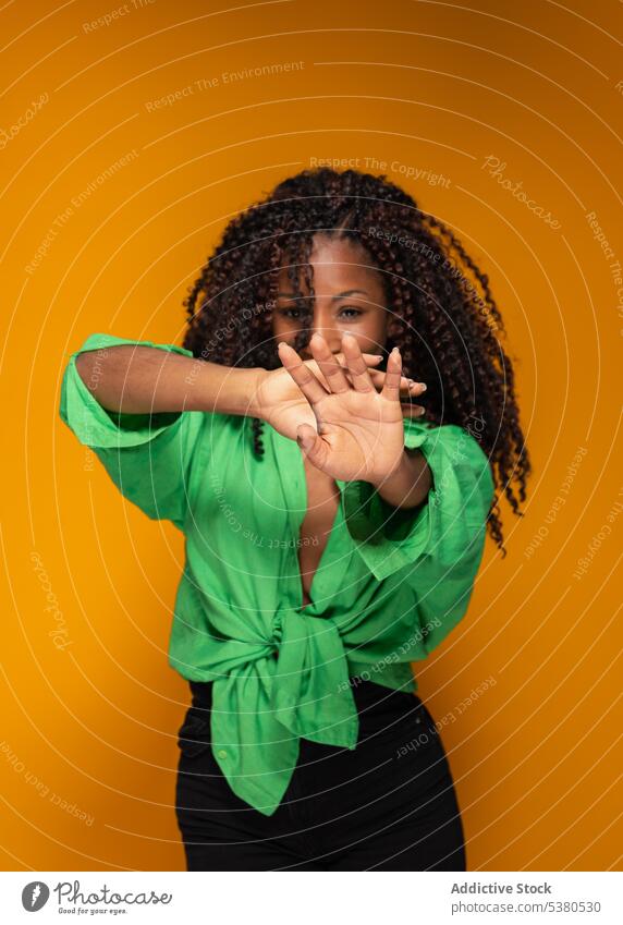 Trendige schwarze Frau mit erhobenen Armen im Studio gestikulieren Zeichen krause Haare trendy modern Stil Symbol lässig Mundabdeckung jung Afroamerikaner Dame