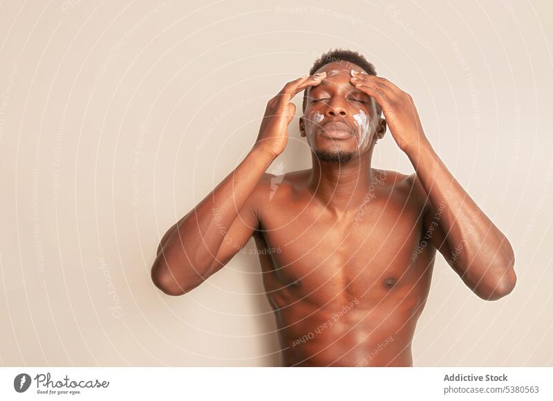 Schwarzer Mann ohne Hemd cremt sein Gesicht ein Hautpflege Sahne bewerben täglich Feuchtigkeit Kosmetologie Verfahren Gesichtsbehandlung Routine Leckerbissen