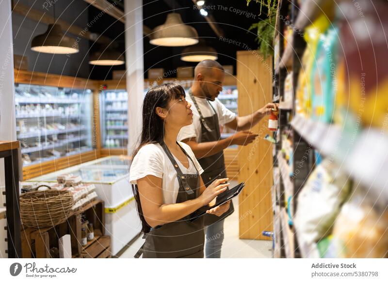 Ethnisches Verkaufspersonal prüft Tablette für Lebensmittel im Regal Frau Mann Personal Werkstatt Ware Laden untersuchen männlich prüfen Arbeit Dienst Job