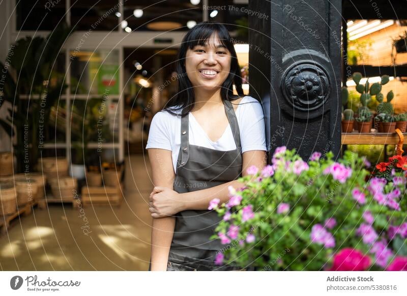 Fröhliche asiatische Frau steht in der Nähe von blühenden Blumen Blumenhändler Lächeln Floristik Arbeit Werkstatt Besitzer Abfertigungsschalter Blumenstrauß