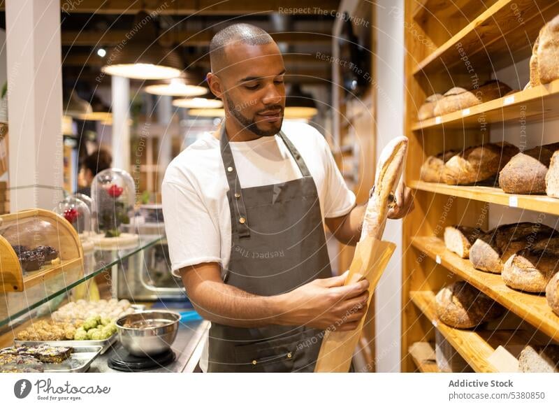 Ernster schwarzer Mann legt Brot in Papiertüte Bäckerei Verkäufer Tüte Lebensmittelgeschäft Werkstatt Kleinunternehmen Arbeit gebacken Besitzer Personal