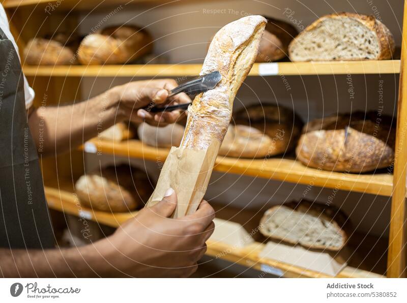 Unbekannter schwarzer Mann legt Brot in Papiertüte anonym Bäckerei Verkäufer Tüte Lebensmittelgeschäft Werkstatt Kleinunternehmen Arbeit gebacken Besitzer