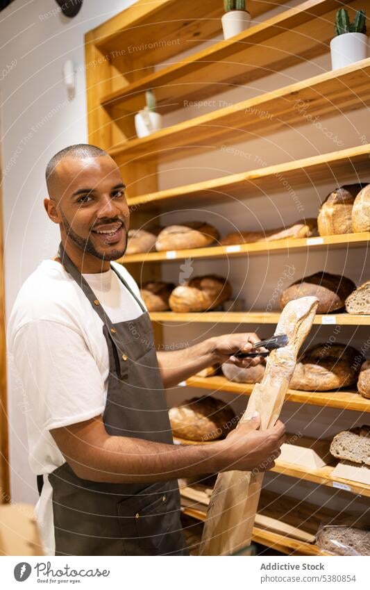Glücklicher schwarzer Mann legt Brot in Papiertüte Bäckerei Verkäufer Tüte Lebensmittelgeschäft Werkstatt Kleinunternehmen Arbeit gebacken Besitzer Personal