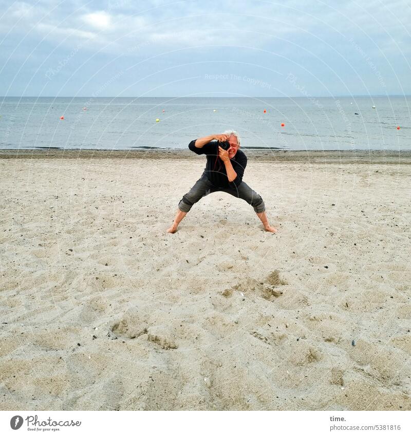 Mann am Strand, fotografierend Ostsee Fotograf Sand Meer Horizont Himmel Haltung barfußlachen gebückt stehen grauhaarig Körperhaltung gute Laune Spaß Küste
