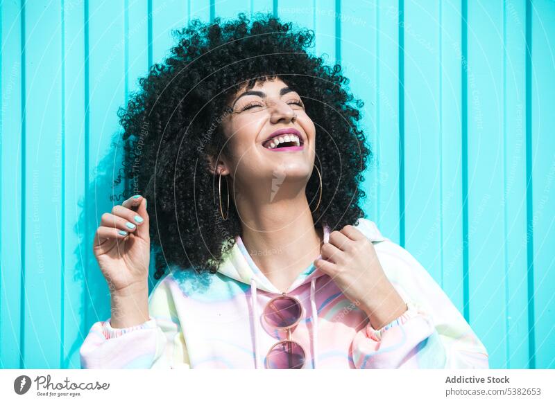Fröhliche ethnische Frau lachend auf blauem Hintergrund Lachen Spaß Mode heiter Glück Vorschein Frisur Schatten Wand Sommer jung hispanisch Stil Outfit
