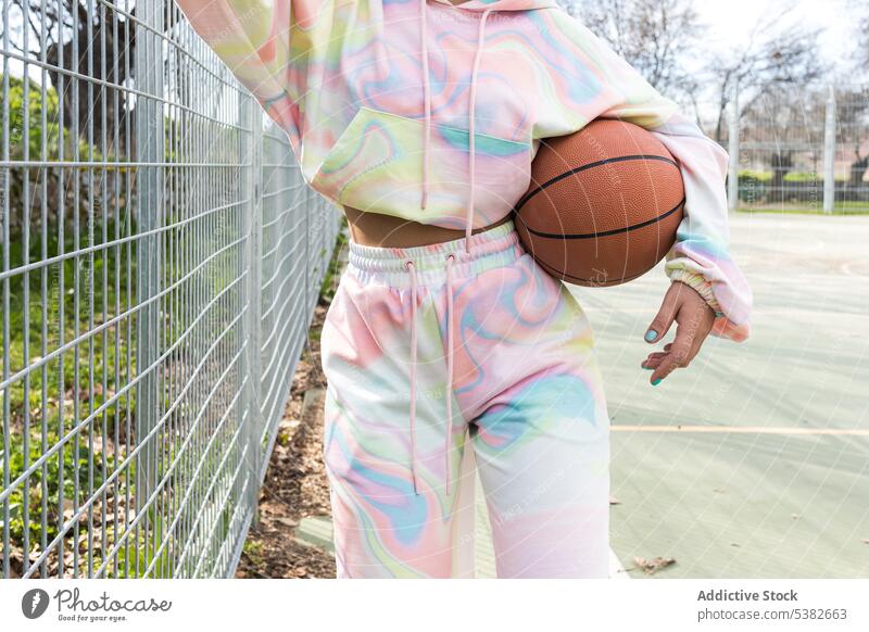 Anonyme Frau mit Basketball am Zaun stehend Spieler Sportpark Kapuzenpulli üben Athlet Training Tageslicht jung Hobby Sportkleidung Übung tagsüber Jugend Outfit