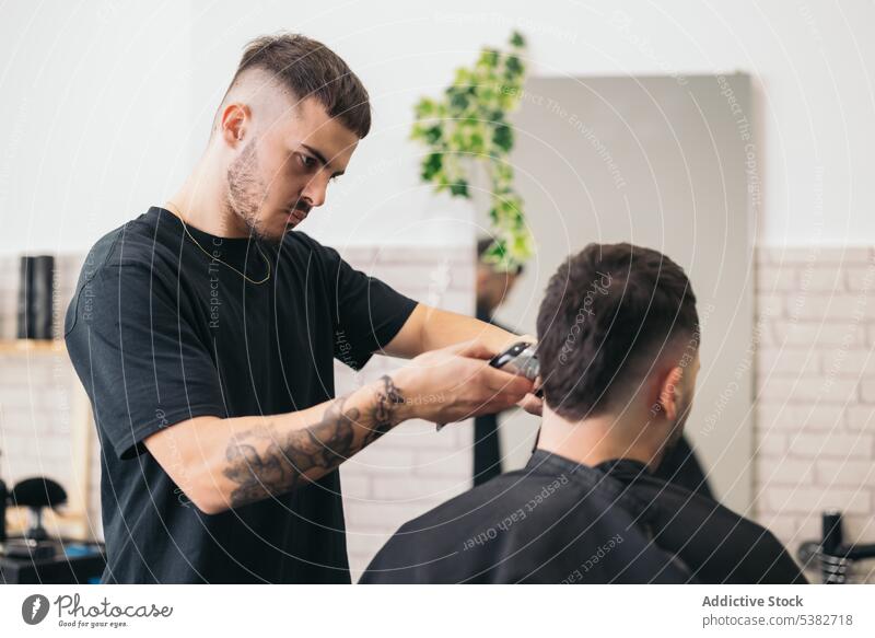 Junger Friseur schneidet Haare mit Maschine im Friseursalon Barbershop Vollbart bärtig Bartiger Mann Schönheit Klinge Pflege Klient Ausschnitt Frisur Kamm