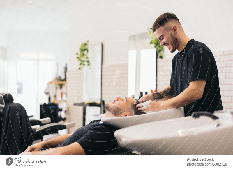 Junger Friseur wäscht Haare im Friseursalon Erwachsener Amerikaner Barbershop Vollbart Schönheit Business Pflege Kaukasier Klient Frisur Konditionierer Gesicht