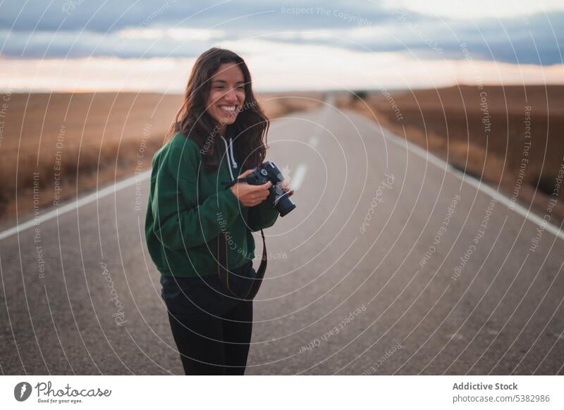 Junge Frau mit Fotokamera auf der Straße stehend Fotoapparat Fotograf Natur Lächeln Gerät Fotografie fotografieren positiv jung Hobby Landschaft lässig Asphalt