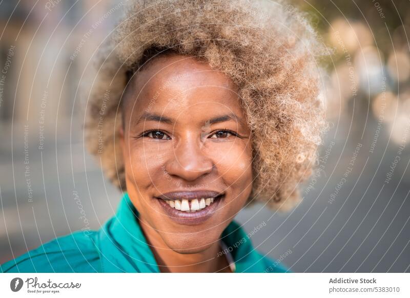 Lächelnde schwarze Frau mit lockigem Haar auf der Straße Porträt positiv heiter Glück krause Haare Inhalt Stil Großstadt Vorschein Afroamerikaner ethnisch