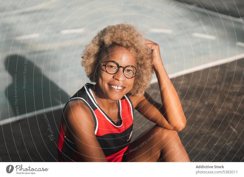 Fröhliche schwarze Sportlerin, die sich auf dem Sportplatz ausruht Athlet Basketball Gericht Sportbekleidung Sportpark heiter Glück ruhen sportlich Turnschuh