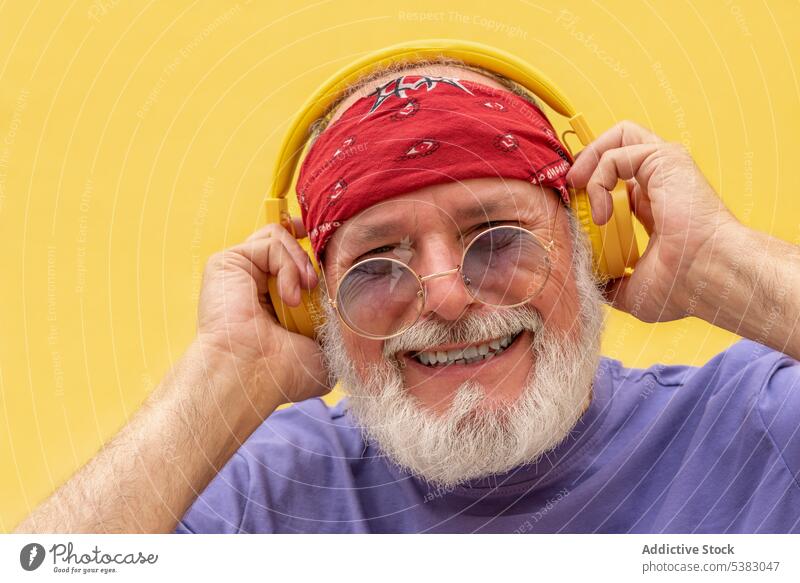 Glücklicher Mann mit Kopfhörern und Brille, der Musik hört heiter zuhören Hipster Porträt Apparatur Schal positiv Melodie Senior Vollbart männlich Klang meloman