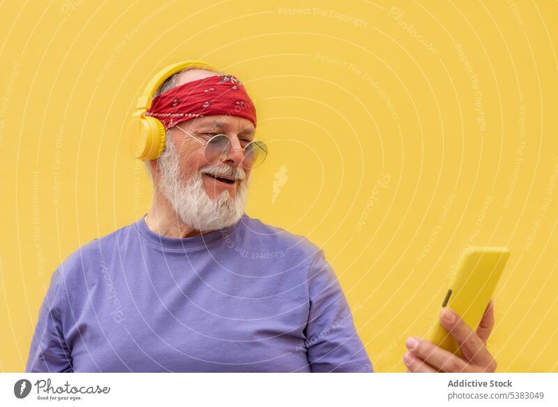Älterer Mann mit Kopfhörern und Smartphone Audio Vollbart unterhalten Gesang Mobile gestikulieren Melodie Telefon sich[Akk] bewegen positiv Glück Studioaufnahme